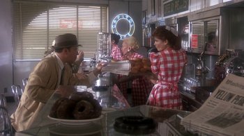 Movie still from “Blaze” (1989), directed by Ron Shelton – A group of people standing around a counter; Wide shot, Over the shoulder angle