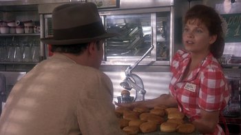 Movie still from “Blaze” (1989), directed by Ron Shelton – A man and a woman in front of a counter with donuts; Medium shot, Over the shoulder angle