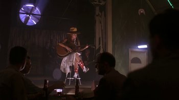 Movie still from “Blaze” (1989), directed by Ron Shelton – A man sitting on a stool playing a guitar; Wide shot, Low angle