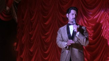 Movie still from “Blaze” (1989), directed by Ron Shelton – A man wearing a suit and bow tie holding a microphone; Medium shot, Low angle