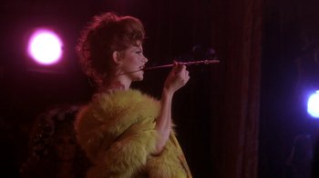Movie still from “Blaze” (1989), directed by Ron Shelton – A woman in a yellow fur coat holding a flute; Close Up shot, Over the shoulder angle