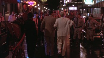 Movie still from “Blaze” (1989), directed by Ron Shelton – A group of people walking down a street at night; Wide shot, Over the shoulder angle