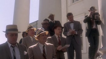 Movie still from “Blaze” (1989), directed by Ron Shelton – A group of men in suits and hats standing next to each other in front of a building; Medium shot, Low angle