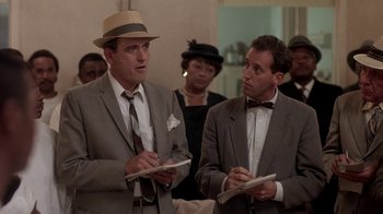 Movie still from “Blaze” (1989), directed by Ron Shelton – A couple of men standing next to each other in a room; Medium shot, Low angle