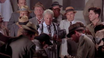 Movie still from “Blaze” (1989), directed by Ron Shelton – A group of men standing next to each other in front of microphones; Medium shot, High angle