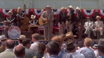 Movie still from “Blaze” (1989), directed by Ron Shelton – A group of men in cowboy hats sing on stage; Wide shot, High angle
