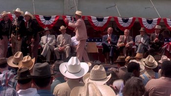 Movie still from “Blaze” (1989), directed by Ron Shelton – A man in a cowboy hat is on a stage; Wide shot, Over the shoulder angle