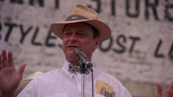 Movie still from “Blaze” (1989), directed by Ron Shelton – An older man wearing a hat is speaking into a microphone; Close Up shot, Low angle
