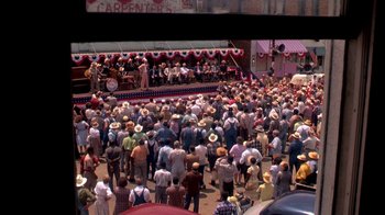 Movie still from “Blaze” (1989), directed by Ron Shelton – A crowd of people standing on a street; Extreme Wide shot, High angle