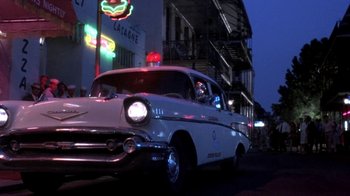 Movie still from “Blaze” (1989), directed by Ron Shelton – An old car is parked on the side of the street; Wide shot, Low angle
