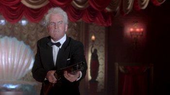 Movie still from “Blaze” (1989), directed by Ron Shelton – An older man in a tuxedo holding a gun; Medium shot, Low angle