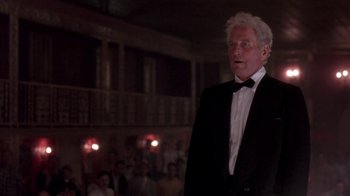 Movie still from “Blaze” (1989), directed by Ron Shelton – An older man wearing a tuxedo standing in front of an audience; Medium shot, Low angle