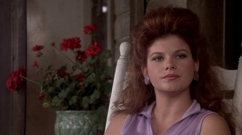 Movie still from “Blaze” (1989), directed by Ron Shelton – A person sitting in a chair near a flower pot; Close Up shot, Over the shoulder angle