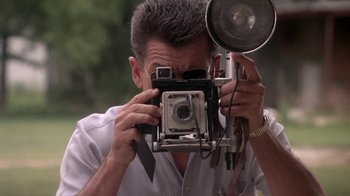 Movie still from “Blaze” (1989), directed by Ron Shelton – A man taking a picture with an old fashioned camera; Close Up shot, Low angle