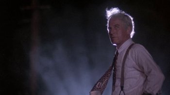 Movie still from “Blaze” (1989), directed by Ron Shelton – An older man wearing a tie standing in front of smoke; Medium shot, Low angle