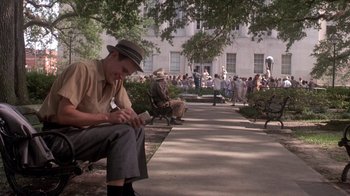 Movie still from “Blaze” (1989), directed by Ron Shelton – A man sitting on top of a bench next to trees; Wide shot, Low angle