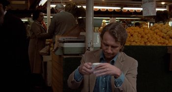 Movie still from “Body Double” (1984), directed by Brian De Palma – A man holding a coffee cup while standing in a store; Medium shot, Over the shoulder angle