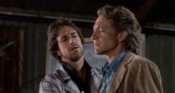 Movie still from “Body Double” (1984), directed by Brian De Palma – Two men standing next to each other in front of a chalkboard; Close Up shot, Over the shoulder angle