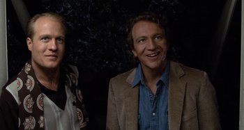 Movie still from “Body Double” (1984), directed by Brian De Palma – A man and a woman standing next to each other in front of a tree; Close Up shot, Low angle