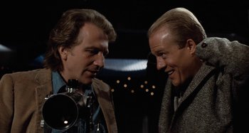 Movie still from “Body Double” (1984), directed by Brian De Palma – Two men talking to each other in front of a camera; Close Up shot, Low angle