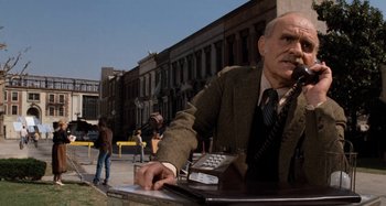 Movie still from “Body Double” (1984), directed by Brian De Palma – An older man sitting at a table with a phone; Medium shot, Low angle