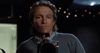 Movie still from “Body Double” (1984), directed by Brian De Palma – A man in a blue sweater is holding a camera; Close Up shot, Low angle