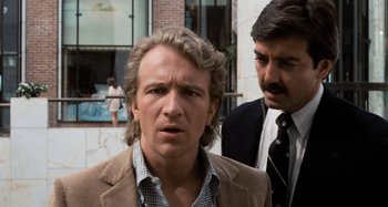 Movie still from “Body Double” (1984), directed by Brian De Palma – A man in a suit and tie next to another man in a suit and tie; Close Up shot, Over the shoulder angle