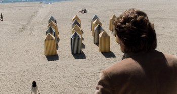 Movie still from “Body Double” (1984), directed by Brian De Palma – A woman standing on the beach looking at a row of yellow and blue beach chairs; Extreme Wide shot, High angle