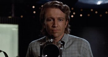 Movie still from “Body Double” (1984), directed by Brian De Palma – A man with long blonde hair is holding a camera; Close Up shot, Low angle