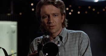 Movie still from “Body Double” (1984), directed by Brian De Palma – A man holding a camera in front of a wall; Close Up shot, Low angle