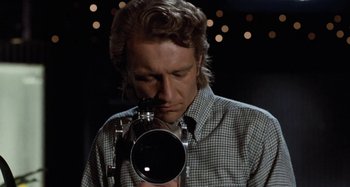 Movie still from “Body Double” (1984), directed by Brian De Palma – A man holding a video camera up to his face; Close Up shot, Low angle