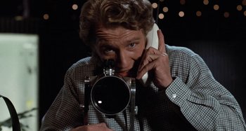 Movie still from “Body Double” (1984), directed by Brian De Palma – A man holding a camera while talking on a phone; Close Up shot, Low angle