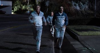 Movie still from “Body Double” (1984), directed by Brian De Palma – Three men are running on the sidewalk at night; Wide shot, High angle