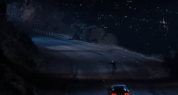 Movie still from “Body Double” (1984), directed by Brian De Palma – A person standing on the side of a road at night; Extreme Wide shot, High angle