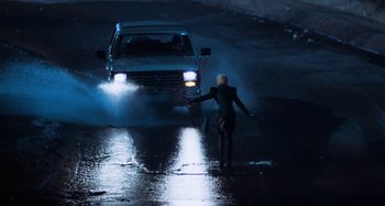 Movie still from “Body Double” (1984), directed by Brian De Palma – A woman is walking in the rain near a car; Wide shot, High angle