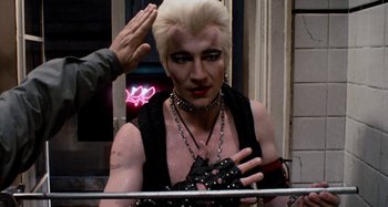 Movie still from “Body Double” (1984), directed by Brian De Palma – A man with white blonde hair and a black shirt is saluting; Close Up shot, Over the shoulder angle