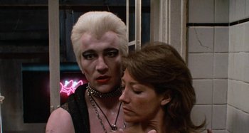 Movie still from “Body Double” (1984), directed by Brian De Palma – A man and a woman standing next to each other in front of a neon sign; Close Up shot, Over the shoulder angle