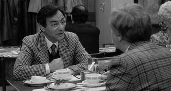 Movie still from “Broadway Danny Rose” (1984), directed by Woody Allen – An older man sitting at a dinner table talking to a younger man; Medium shot, Over the shoulder angle
