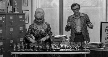 Movie still from “Broadway Danny Rose” (1984), directed by Woody Allen – A man and a woman standing in front of wine glasses on a table; Medium shot, Over the shoulder angle