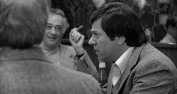 Movie still from “Broadway Danny Rose” (1984), directed by Woody Allen – A man sitting in a room with another man in a suit; Close Up shot, Over the shoulder angle