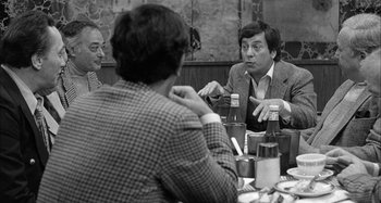 Movie still from “Broadway Danny Rose” (1984), directed by Woody Allen – A group of people sitting at a table talking to each other; Medium shot, Over the shoulder angle