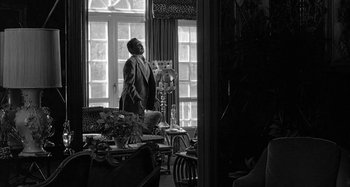 Movie still from “Broadway Danny Rose” (1984), directed by Woody Allen – A black and white photo of a man standing in a living room; Wide shot, Low angle