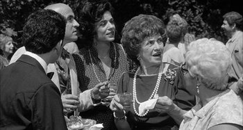 Movie still from “Broadway Danny Rose” (1984), directed by Woody Allen – A black and white photo of a group of people at an outdoor event; Medium shot, Over the shoulder angle