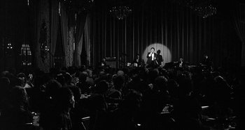 Movie still from “Broadway Danny Rose” (1984), directed by Woody Allen – A black - and - white photo of a crowd of people in front of a microphone; Extreme Wide shot, High angle