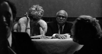 Movie still from “Broadway Danny Rose” (1984), directed by Woody Allen – An older man and woman sitting at a dinner table; Medium shot, Over the shoulder angle