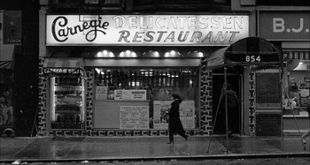 Movie still from “Broadway Danny Rose” (1984), directed by Woody Allen – A woman walking down the sidewalk in front of a restaurant; Extreme Wide shot, High angle
