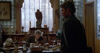 Movie still from “Butch and Sundance: The Early Days” (1979), directed by Richard Lester – Two men sitting at a table in front of a statue; Medium shot, Over the shoulder angle