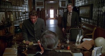 Movie still from “Butch and Sundance: The Early Days” (1979), directed by Richard Lester – A group of men sitting at a table in a room; Medium shot, Over the shoulder angle