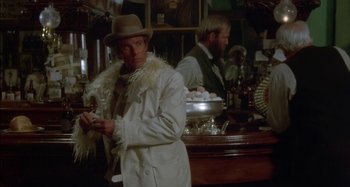 Movie still from “Butch and Sundance: The Early Days” (1979), directed by Richard Lester – A man wearing a white coat and a hat in front of a bar; Medium shot, Over the shoulder angle