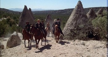 Movie still from “Butch and Sundance: The Early Days” (1979), directed by Richard Lester – A group of men riding horses through the desert; Wide shot, Low angle